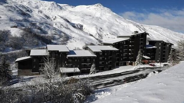 Une montagne enneigée, sur laquelle se trouve un chalet comprenant plusieurs bâtiments et une piste de ski.