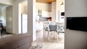 Une cuisine moderne avec des meubles blancs, un coin repas comprenant une table et des chaises, et un téléviseur fixé au mur.