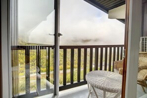 A balcony with a view of a road and greenery, a wicker chair, and a glass door. - Ski-in/ski-out & foot of the slopes, 3rd floor, view mountain, balcony, tv, ski locker, 66m² (Les Menuires)