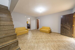 Ein geräumiges Zimmer mit Treppe, zwei gelben Sofas, einer Holztür und einem gefliesten Boden.