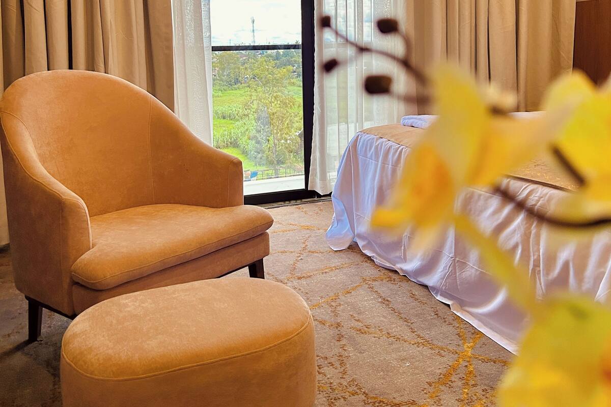 A hotel room with a sofa, a bed, a view of the outdoors, and a window with curtains.