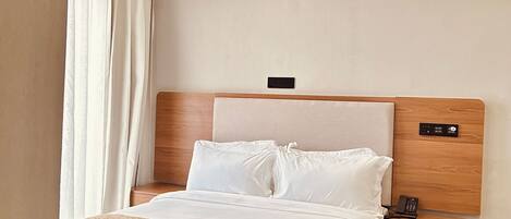 A hotel room with a bed, bedside table, nightstand, and an air conditioning unit.
