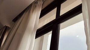 Ein Fenster mit weißen Vorhängen, einem schwarzen Rahmen und Blick auf eine gebirgige Landschaft.