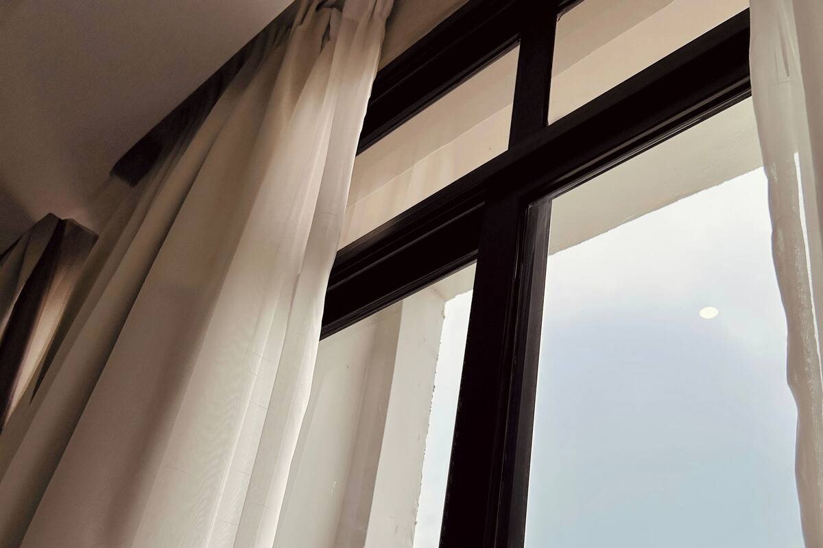 A window with white curtains, a black frame, and a view of a mountainous landscape.