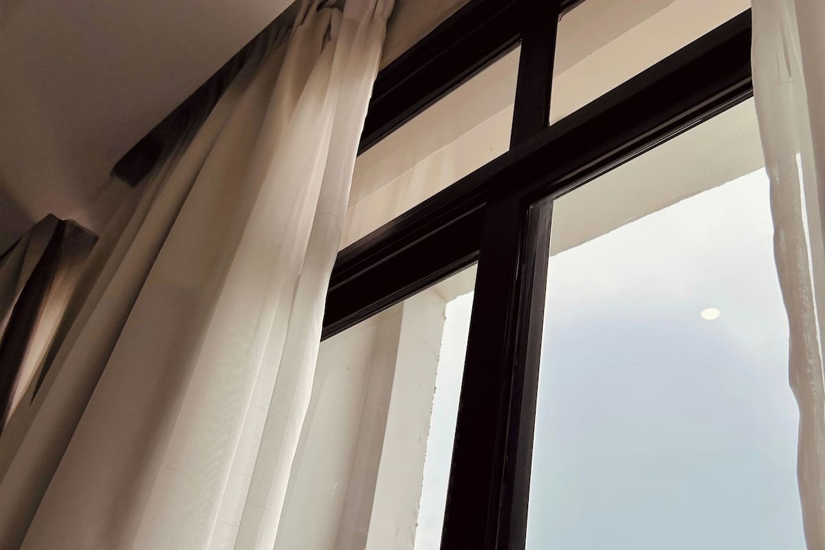 A window with white curtains, a black frame, and a view of a mountainous landscape.