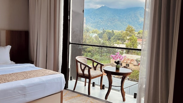 Ein Hotelzimmer mit einem Bett, einem kleinen Tisch mit Stühlen, einem Balkon mit Bergblick und einem Fenster mit Vorhängen.