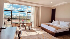 Ein Hotelzimmer mit einem großen Bett, einem Schreibtisch und Blick ins Freie.