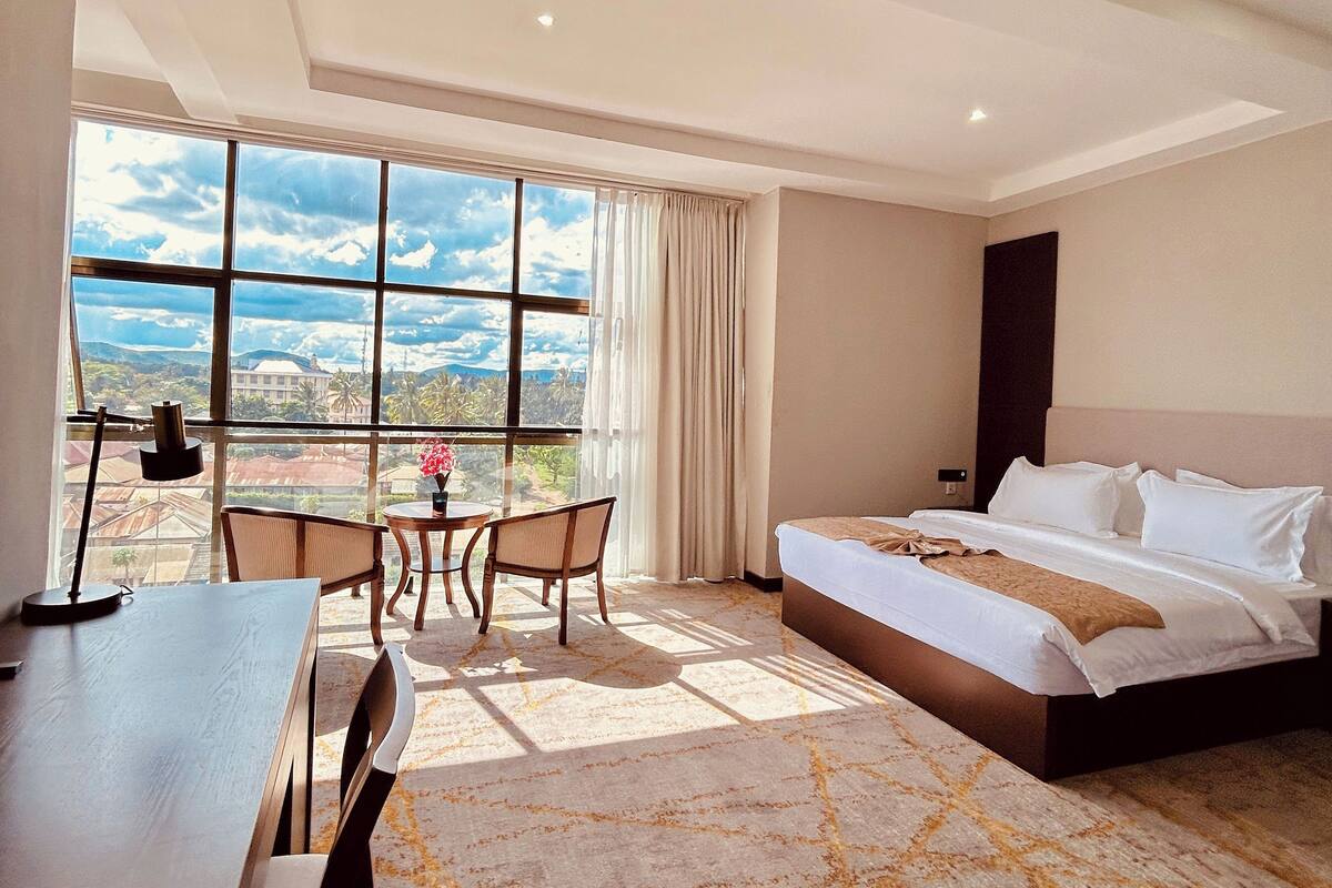 A hotel room with a large bed, a desk, and a view of the outdoors.