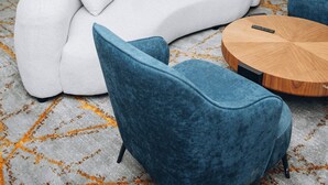 Ein stilvoller Wohnbereich mit einer Couch, zwei Sesseln, einem runden Holztisch und einer Küche im Hintergrund.