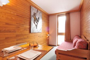 Ein Zimmer mit Holzboden, einem Bett, einem Esstisch gedeckt mit Tellern und Gläsern, und einem Gemälde an der Wand.