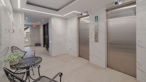 Un ascensor modern amb un panell de control, una paret de marbre i una taula de vidre amb cadires.