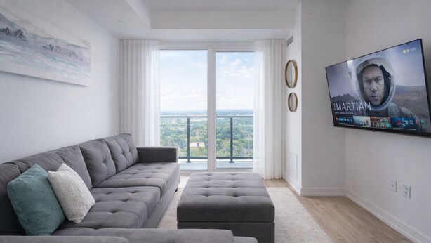 Een moderne woonkamer met een grijze bank, voetenbankje en een flatscreen televisie aan de muur.