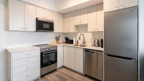 Een moderne keuken met witte kastjes, een roestvrijstalen koelkast, een magnetron, een oven en een vaatwasser.