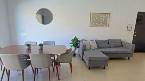 A modern living room with a dining table, chairs, a grey sofa, a round mirror, and a framed artwork on the wall. - Nice condo in quiet area 5 minutes from downtown! (Cabo San Lucas)