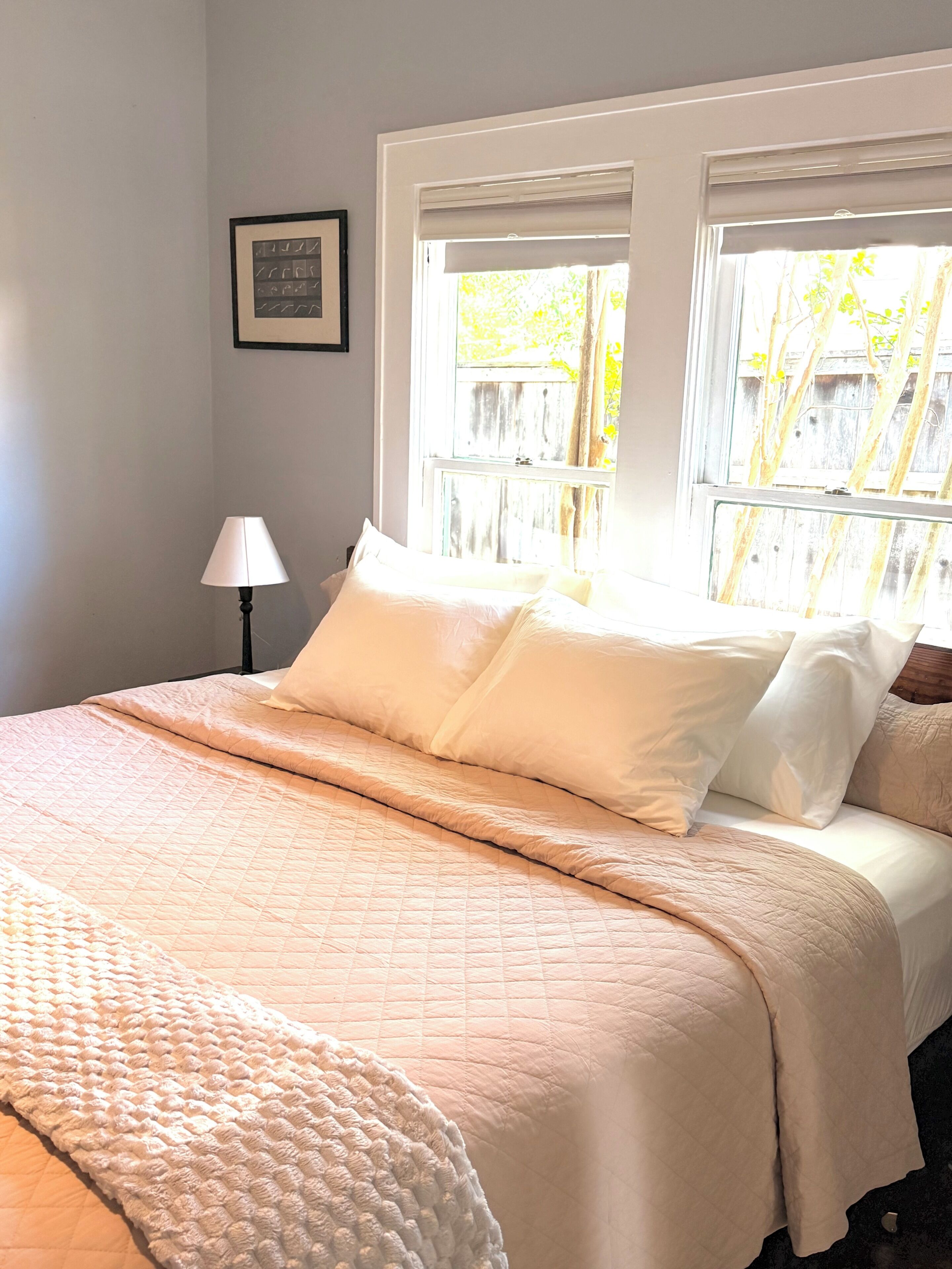 A bed with white bedding, a lamp, and a window with a view of trees.