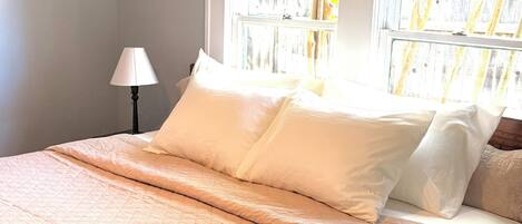 A bed with white bedding, a lamp, and a window with a view of trees.