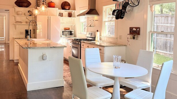A modern kitchen with white cabinetry, a central island, and a dining area with white chairs.