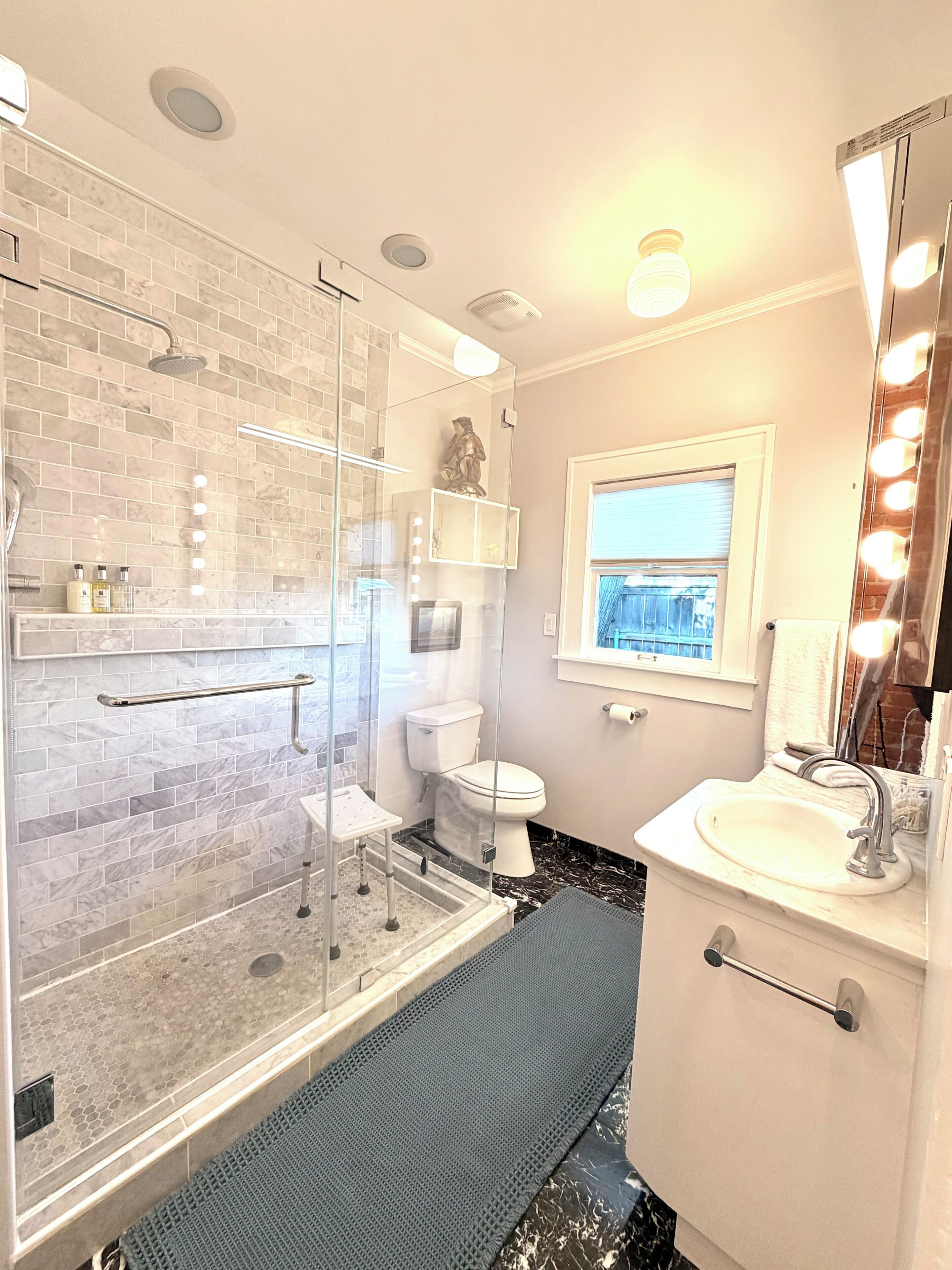 A bathroom with a glass shower enclosure, a toilet, a sink with a vanity, and a mirror with lights.