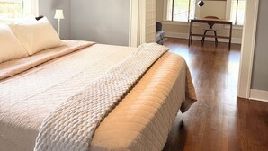A bedroom with a large bed, a ceiling fan, and a view to a dining area.