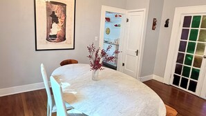 A dining area with a white table, white chairs, a chandelier, and a framed picture on the wall.