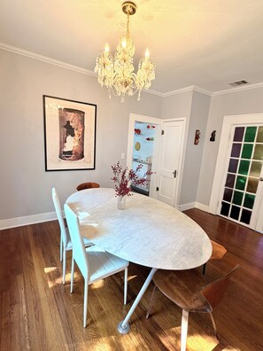A dining area with a white table, white chairs, a chandelier, and a framed picture on the wall.