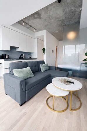 Ein zeitgemäßer Wohnraum mit einem grauen Ecksofa, einem runden Couchtisch und einer Küchenzeile im Hintergrund.
