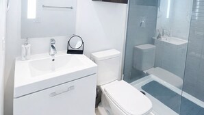 Ein modernes Badezimmer mit einem weißen Waschtisch, einer Toilette, einer Duschkabine aus Glas und einem dunklen Holzschrank.