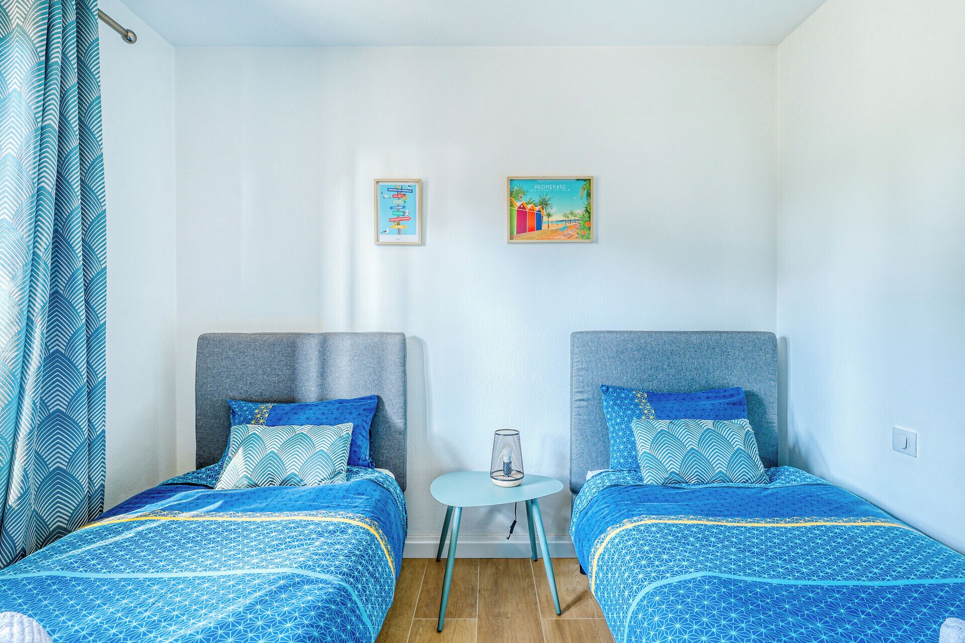 Una habitación con dos camas, una mesita pequeña y dos cuadros en la pared.