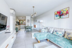 A modern living room with a sofa, a dining area, and a kitchen in the background. - Stunning modern 2BR with pool, 5-min walk to beach (Bormes-les-Mimosas)
