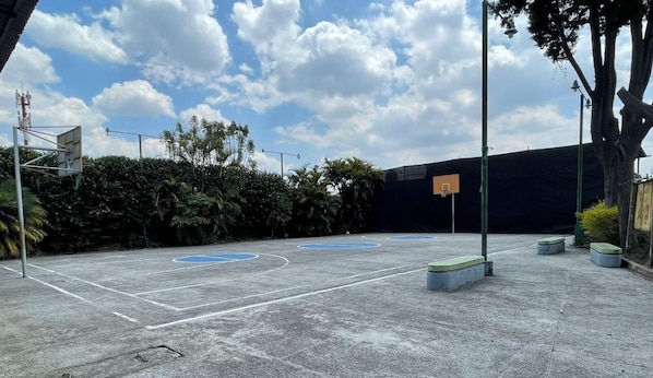 Un terrain de basket-ball en plein air, équipé d’un panier de basket, de bancs et d’une clôture.