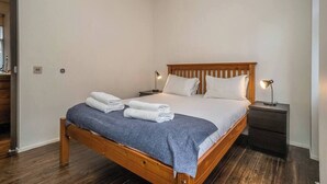 Habitación individual con una cama de madera, una mesita de noche con lámpara y una colcha azul.