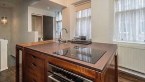 Una cocina moderna con una isla central, horno empotrado y una ventana con cortinas translúcidas.
