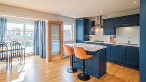 Une cuisine moderne avec des meubles bleus, un îlot en marbre et un coin repas doté de chaises en bois.