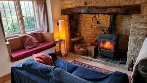 A cozy room with a stone fireplace, a sofa, a table with a lamp, and a window with curtains. - 18th Century Cotswolds Cottage | Parking | Garden - Pass the Keys (Bourton-on-the-Water)