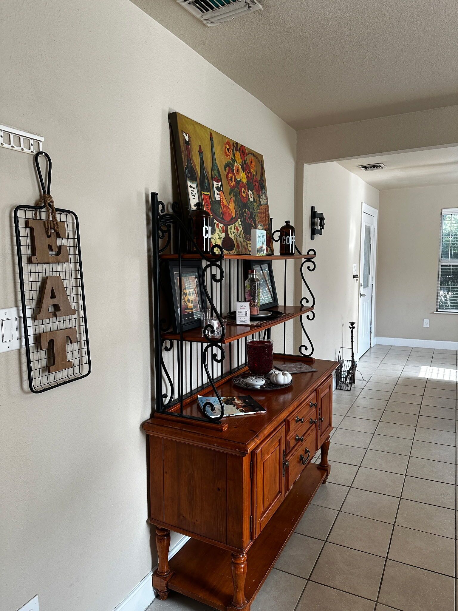A spacious room with a wooden cabinet, a wall-mounted picture, and a decorative metal rack.