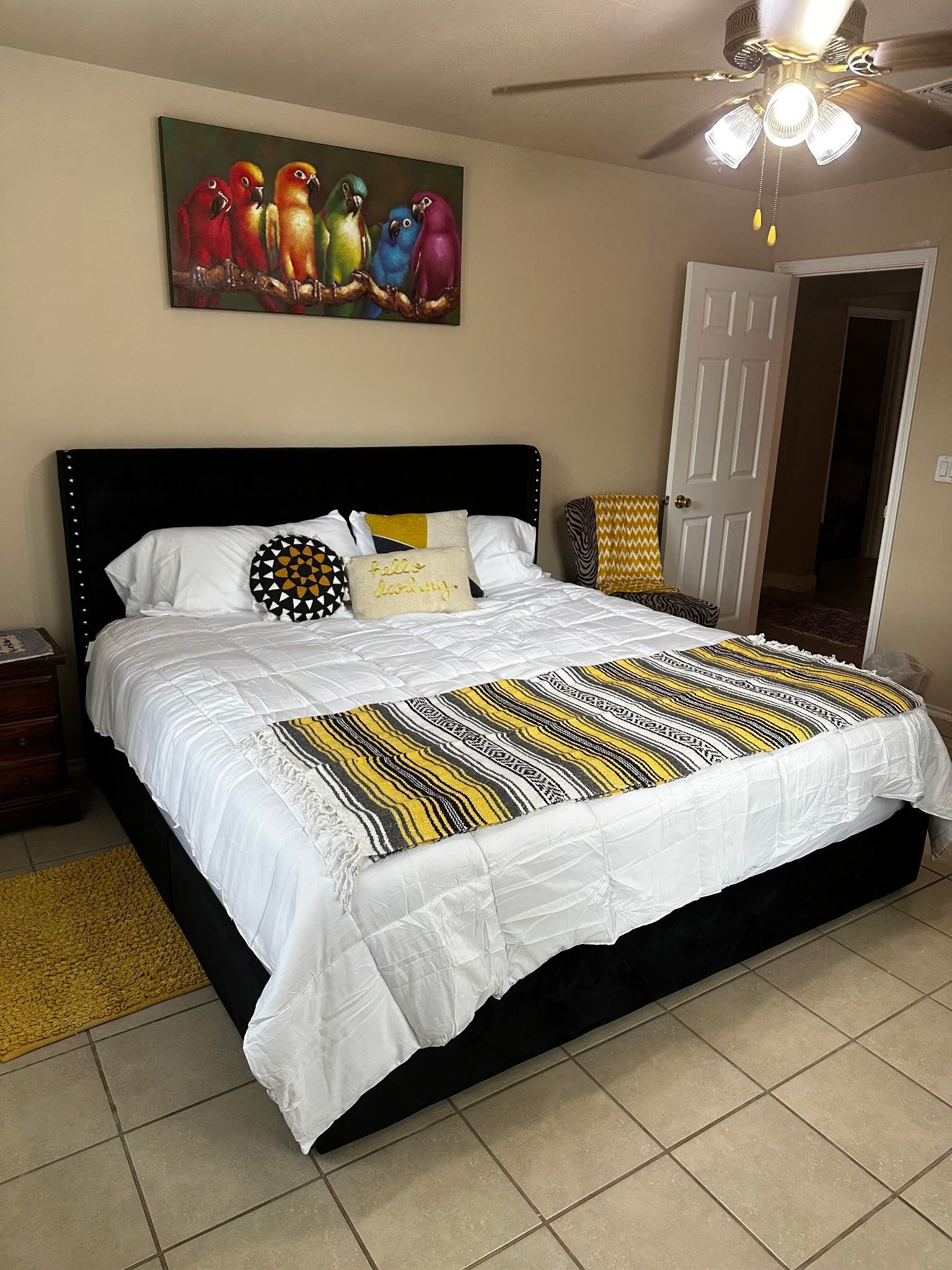 A bedroom with a bed, a ceiling fan, a door, and a painting on the wall.