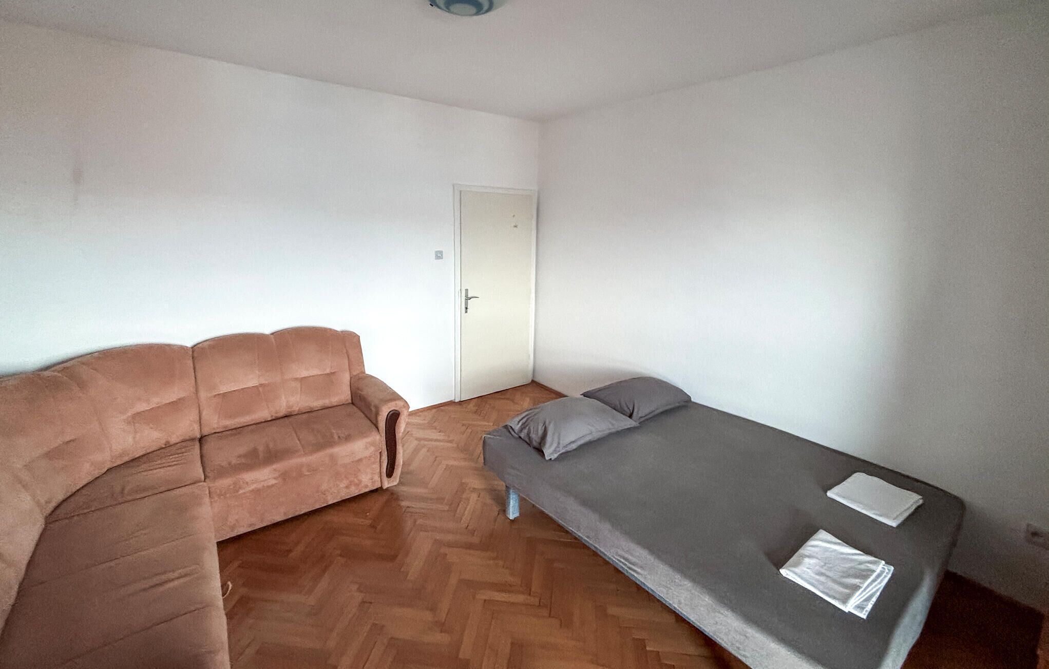 A small, sparsely furnished room with a brown sofa and a single bed.