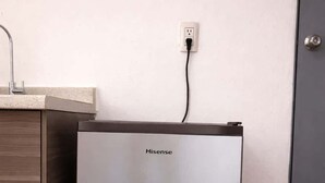 A compact, modern refrigerator with a Hisense logo, positioned next to a wooden cabinet and a wall socket. - Milan Providencia, Private Apartment (Guadalajara)
