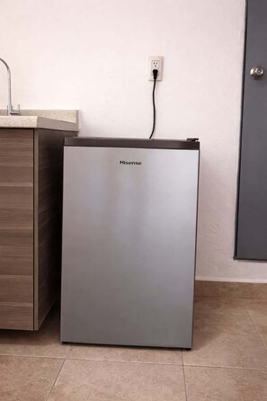 A compact, modern refrigerator with a Hisense logo, positioned next to a wooden cabinet and a wall socket. - Milan Providencia, Private Apartment (Guadalajara)
