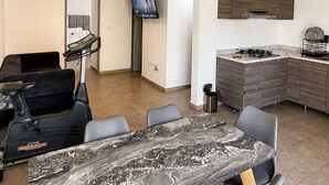 A modern living room with a marble dining table, black chairs, a sofa, a TV, and a kitchen area with a stove and cabinets. - Milan Providencia, Private Apartment (Guadalajara)