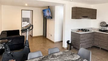 A modern living room with a marble dining table, black chairs, a sofa, a TV, and a kitchen area with a stove and cabinets.
