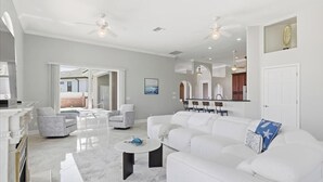 A spacious living room with a white sofa, a coffee table, and a dining area with a bar. - Luxury Riverfront Retreat with Pool & Hot Tub (Cape Coral)