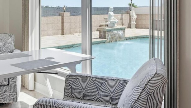 A modern outdoor pool area with a view of the sea, a dining table, and patterned furniture. - Luxury Riverfront Retreat with Pool & Hot Tub (Cape Coral)
