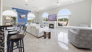 A spacious living area with a white sofa, a patterned armchair, a fireplace, and a television. - Luxury Riverfront Retreat with Pool & Hot Tub (Cape Coral)