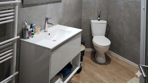 A modern bathroom with a white sink, mirror, and toilet, grey tiled walls, and a wooden floor. - Ideal accommodation for families 5 min from Tourcoing ouigo station (Tourcoing)