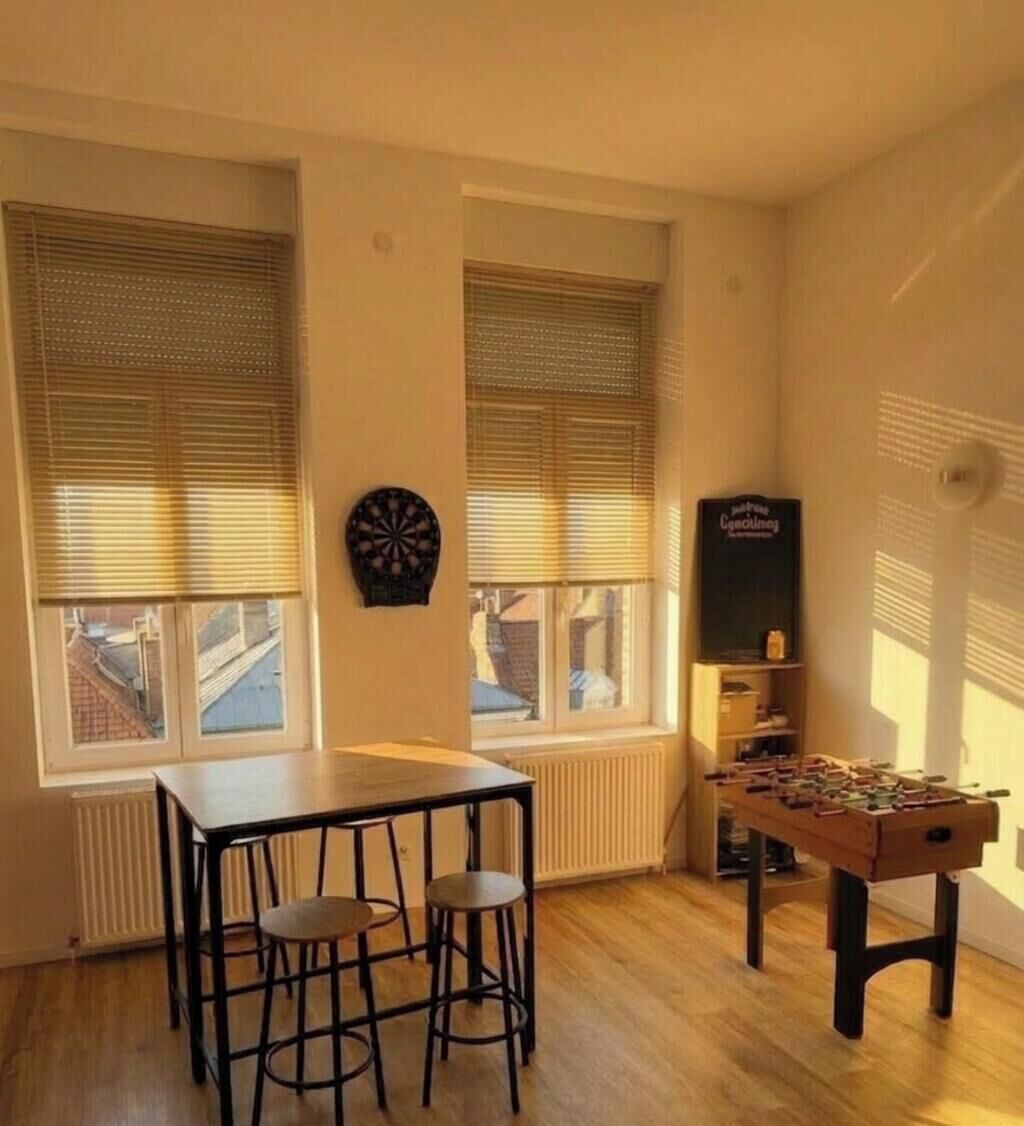 Ein Raum mit Tisch, Stühlen, einer Dartscheibe, einem Kicker und einer weiteren Dartscheibe an der Wand.