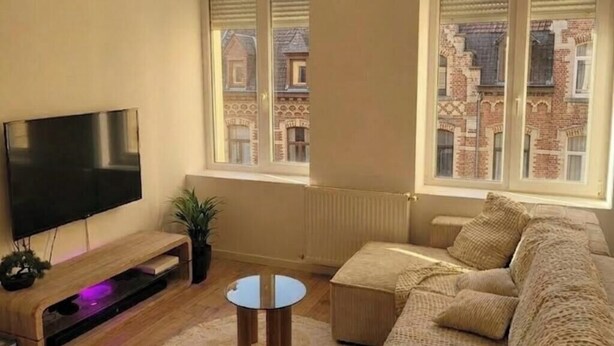 A living room with a TV, sofa, and windows overlooking a building. - Ideal accommodation for families 5 min from Tourcoing ouigo station (Tourcoing)