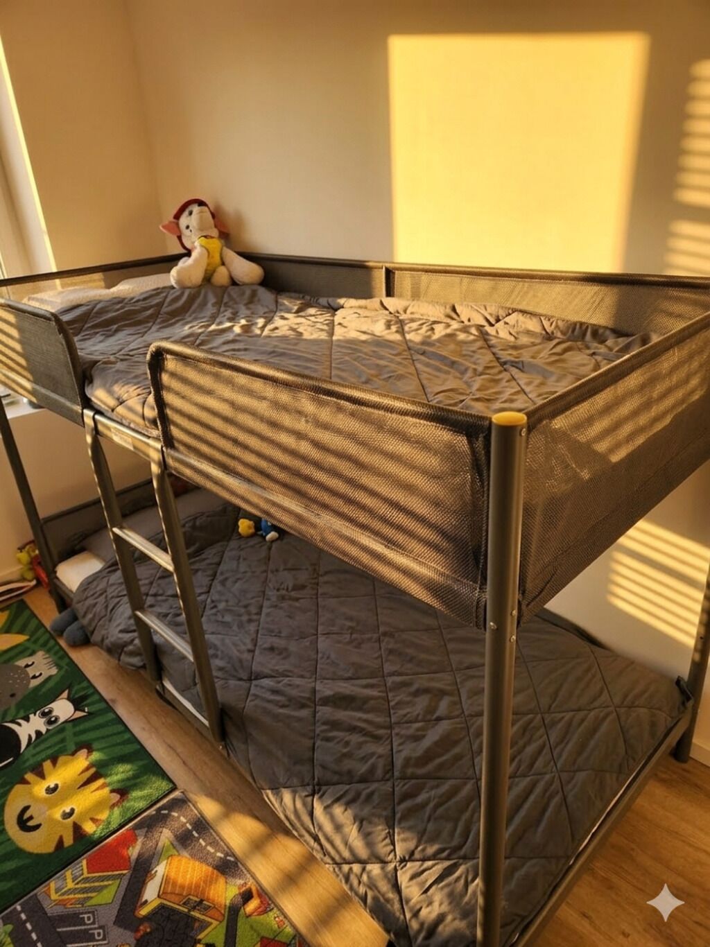 A bunk bed with a grey quilted mattress, metal frame, and a small stuffed toy on the top bunk.