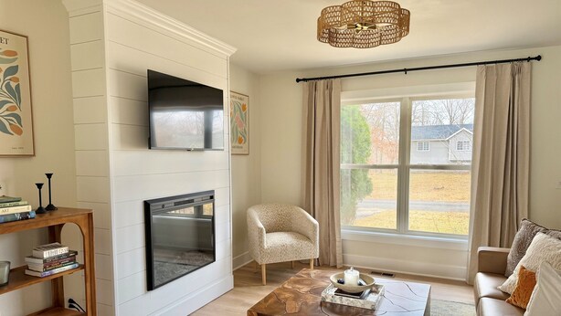 Una sala de estar con chimenea, televisor, sofá, mesa de centro y una ventana con cortinas.