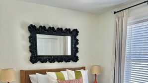 Un dormitorio con cama de madera, ropa de cama blanca, una manta de piel, un espejo con marco negro y dos lámparas de noche.